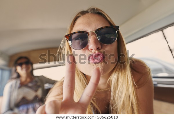 Beautiful girl pulling funny face peace\
sign on road trip in vintage camper van with\
friend
