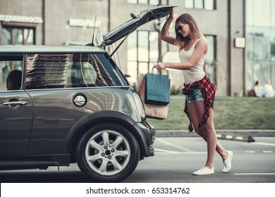 Beautiful Girl Is Putting Shopping Bags Into Car Trunk And Smiling