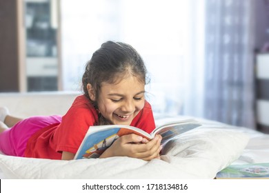 Beautiful girl reading book and smiling. Girl wearing red T-shirt, studying at home with books and doing school homework. Smiling girl.