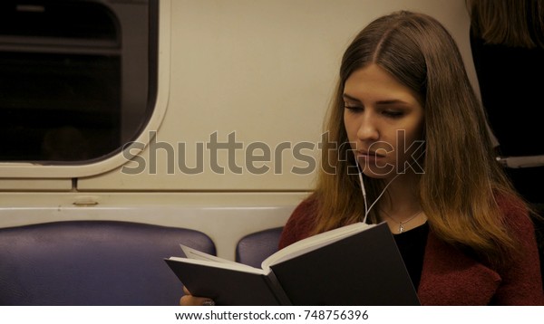 Beautiful girl reading a book\
in train at the subway. Teenager girl read a book in train or\
subway car