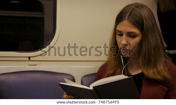 Beautiful girl reading a book\
in train at the subway. Teenager girl read a book in train or\
subway car