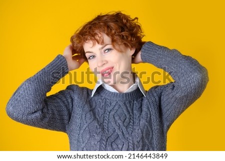 A beautiful girl with red curly hair on a yellow background smiles broadly.