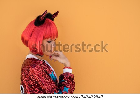 Beautiful girl in red devil costume standing against the wall in anticipation of Halloween. Wears a red wig and horns. The concept of color