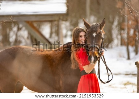 A beautiful girl in a red dress hugs a horse in the rays of the setting sun
