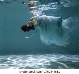 beautiful girl with red hair in a ball gown blue dress underwater on a blue background - Powered by Shutterstock