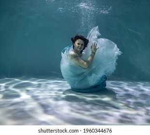 beautiful girl with red hair in a ball gown blue dress underwater on a blue background - Powered by Shutterstock