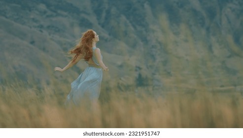 Beautiful girl with red hair in white dress looking at landscape in mountains while wind blows her hair - freedom, inspiration cinematic  - Powered by Shutterstock