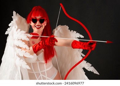 Beautiful girl with red hair, in a white bodysuit, red heart-shaped glasses, red gloves. White wings on the back, traces of kisses on the body. Bow and arrows in hand. Sexy cupid. Smiling