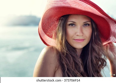 Beautiful girl in a red hat smiling at the summer waterfront