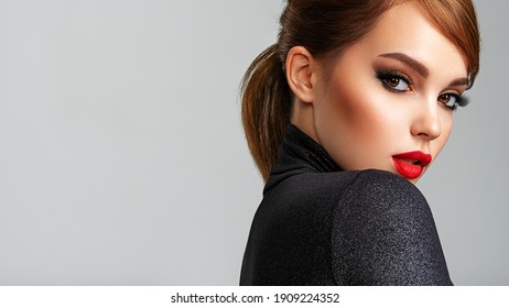 Beautiful girl with red lips and short hair. Pretty face of an young sensual woman. Closeup portrait of a model with bright makeup on a face. Attractive female posing at studio  in black closes.    
