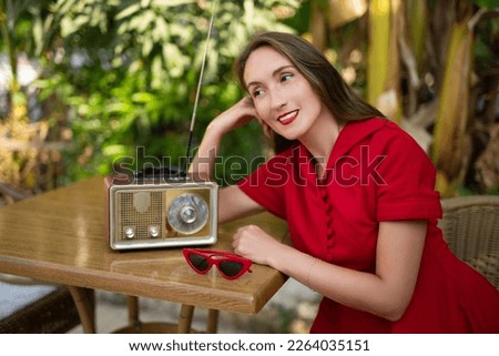 a beautiful girl in a red retro style dress listens to an antique radio