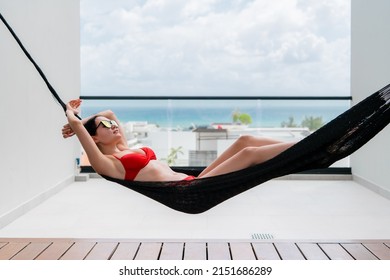 Beautiful Girl Relaxing In A Hammock Over A Pool On A Rooftop Of A Luxury Hotel. View On A Blue Ocean And Sky.