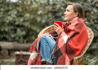 Beautiful girl resting and drinking coffee sitting in autumn garden in chair wrapped in a woolen plaid blanket. copy space - Powered by Shutterstock