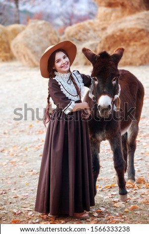 Beautiful girl in retro dress and hat on a donkey farm feeding a donkey. Harvest. Autumn time.
