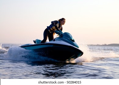 beautiful girl riding her jet skis in the sea at sunset. spray