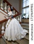  A beautiful girl, in a romantic dress with a low neck, retro style, with dark hair decorated with a white feather.In full growth, goes down the stairs. Historical reconstruction                      