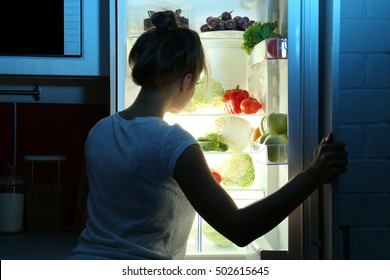 Beautiful girl searching for food in fridge. Hunger concept
