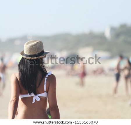 Beautiful girl, seen from behind, with hat who walk on the beach. People in the background. Sabaudia, Lazio, Italy