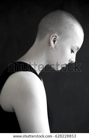 Portrait of a young, very short-haired woman wearing an off-the-shoulder top through which you can see her nipples