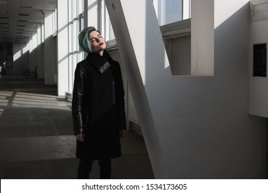 Beautiful girl with short blue fashionable hairstyle in black coat standing in a long corridor standing near column. She looking up, her eyes closed - Shutterstock ID 1534173605