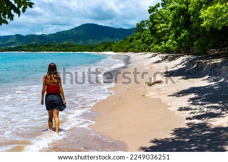 a beautiful girl in a short skirt walks on the famous conchal beach on the pacific coast of Costa Rica; a paradise beach with turquoise water and green hills in the background	
