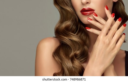 Beautiful girl showing red  manicure nails . makeup and cosmetics. Brunette  girl with long  and   shiny curly hair