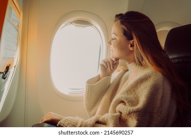 A beautiful girl sits in an airplane at the window and looks at the view. Tourist travel.