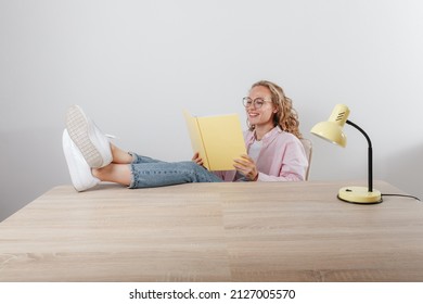 A Beautiful Girl Sits Her Feet Upstairs At The Table And Reads Notes