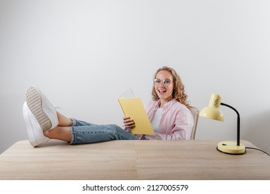 A Beautiful Girl Sits Her Feet Upstairs At The Table And Reads Notes