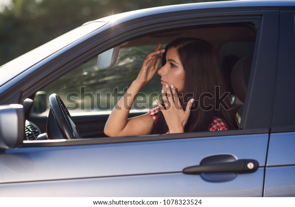 A beautiful girl sits inside a blue car, makes a\
make-up and looks in the mirror while driving. Danger on the road,\
irresponsible driving.