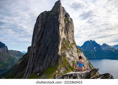 a beautiful girl sits on the rocks enjoying the view of the famous segla mountain in norway, senja island; hesten trail head, the famous norwegian fjords with mighty mountains above the sea