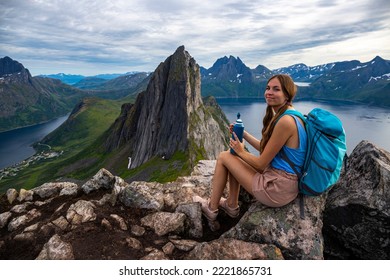 a beautiful girl sits on the rocks enjoying the view of the famous segla mountain in norway, senja island; hesten trail head, the famous norwegian fjords with mighty mountains above the sea