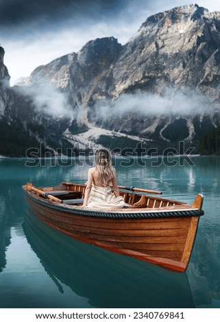 Beautiful girl sitting backwards on a boat on the famous blue lake. Stunning romantic place with typical wooden boats on the alpine lake,(Lago di Braies) Braies lake,Dolomites