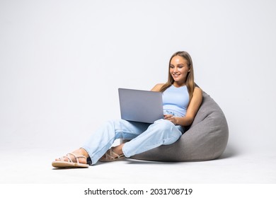 Beautiful Girl Is Sitting On Bean Bag Couch And Is Looking Laptop On White Background.