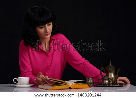 Beautiful girl sitting at a table with a book, a Cup of coffee and an antique service on a dark background