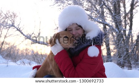 Beautiful girl smiles, caresses her beloved dog in winter in park. girl with a hunting dog walks in winter in forest. dog kisses hostess.