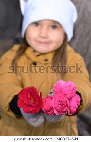 A beautiful girl smiles and holds out peony flowers. Focus on the foreground.