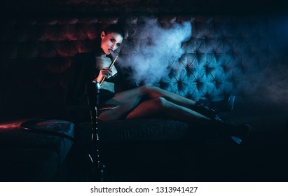 Beautiful Girl smoking hookah in Nightclub. Exhaling smoke. Sexy girl smokes hookah