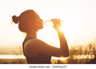 Beautiful Girl In Sportswear Drinks Water From A Bottle At Sunset