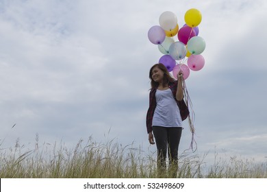 Beautiful girl stand holding balloons in the prairie grass. On a clear day