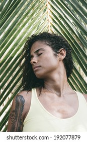 Beautiful Girl Standing Against A Tropical Palm Frond With Her Head Turned To The Side With Closed Eyes And A Serene Expression