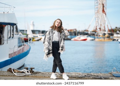 Beautiful girl standing near yacht on pier. Seaport or berth in background. Young woman Wearing casual Outfit posing near water in sunny day. People lifestyle and rest concept. Blurred background - Powered by Shutterstock