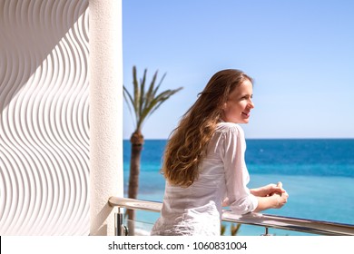The beautiful girl standing on a balcony of apartments looking at the seaside.