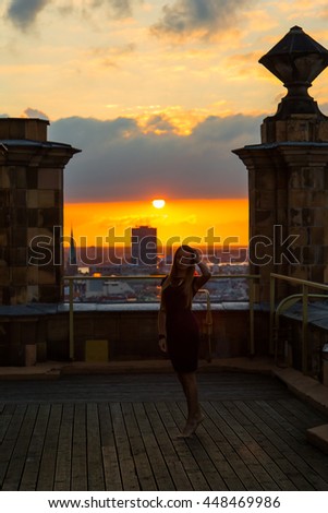 Beautiful girl standing on the roof during sunrise with a stunning Riga view on the background