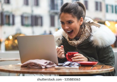 Beautiful Girl Student Checking Her Exam Results On The Computer In A Bar Drinking Coffee - Stunning Young Woman On Her Computer In A Bar In City Center Drinks Coffee While Shopping Online 