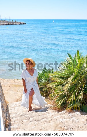 Beautiful girl in a summer dress and hat on the seashore near a background old city europe. Mediterranean Sea, Sitges, Spain.