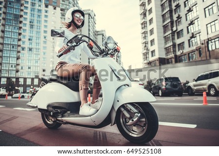 Beautiful girl in sun glasses and helmet is smiling while riding a scooter