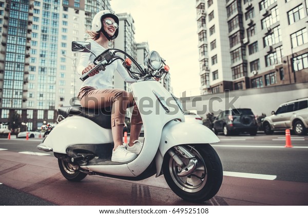 スクーターに乗りながら サングラスとヘルメットをかぶった美しい女の子がにこにこしている の写真素材 今すぐ編集