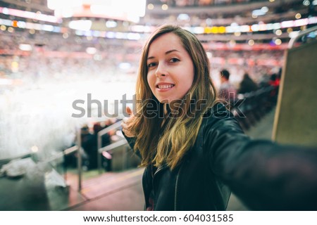 Beautiful girl supporter taking selfie self-portrait while watching basketball game at the stadium