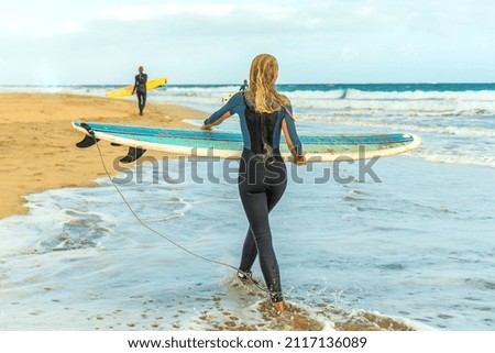 Beautiful girl surfer with a surfboard goes along the sandy beach of the ocean